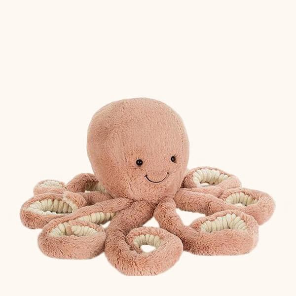 A pink octopus stuffed animal with a smiling face, photographed on a cream background.