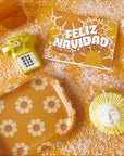 Gold glass phone ornament is featured with a Sunshine Studios flower tray, a 70s Floral "Feliz Navidad" greeting card, a glass sun ornamnet and a pair of Kelso sunglasses.
