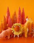 A stuffed animal set inspired by the Savannah. It includes a pink hippo, a red lion with a yellow mane, and a mustard yellow giraffe with orange spots and an orange tail.