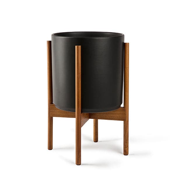 This cylinder pot is solid black and sits within four spokes of a walnut wood plant stand, standing about 7 inches from the ground.