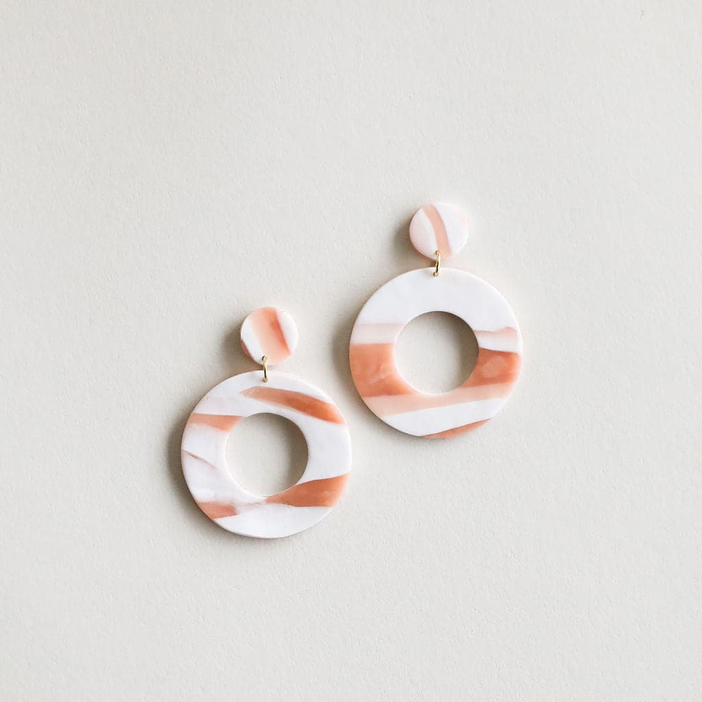 The Mollye earrings that feature a duel circle design. The top circle is smaller and solid while the lower circle is larger and open in the center. This earring features a straight post backing and comes in a variety of colors. This color way is pink, orange and cream.