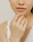 A gold ring with an open front that features a cubic zirconia on one end and a crescent moon on the other, photographed worn on a models hand.