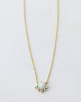 A dainty gold necklace with a round opal pendant in the center that is lined with cz stones around the bottom edge.