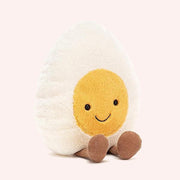A soft stuffed animal in the shape of an egg with yellow yoke face and smiley face, and brown floppy legs.