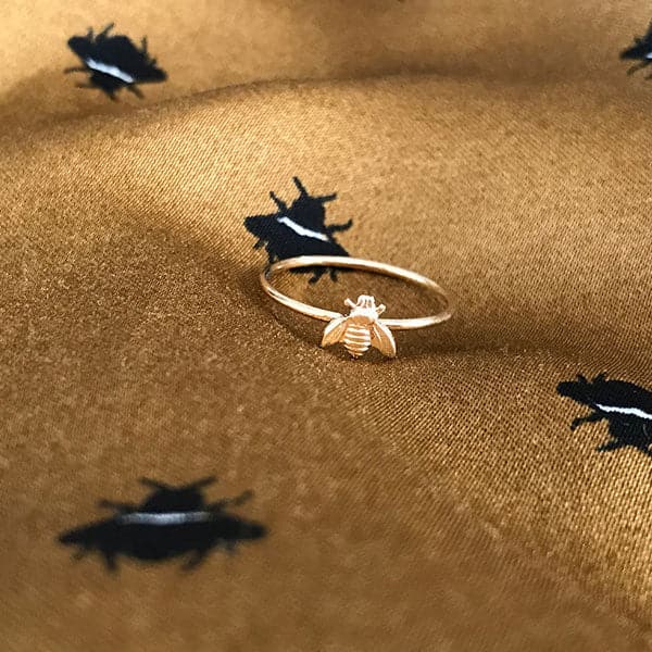 A dainty thin gold band ring with a small gold bee in the center.