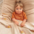 A tan blanket with a mustard yellow sun ray design all over modeled with a toddler.