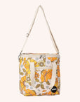 Photographed in front of a yellow background is a mini cooler with a cream adjustable strap and 70's style yellow and orange floral print.
