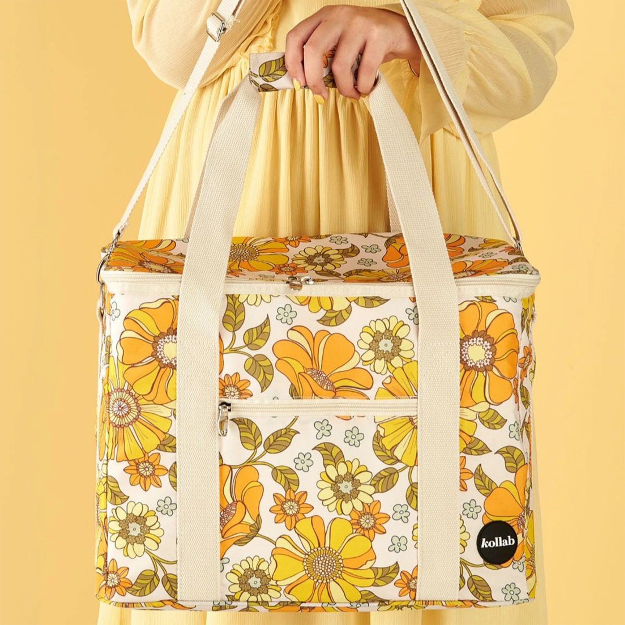Photographed in front of a yellow background is a picnic bag with cream straps and 70&#39;s style yellow and orange floral print. 
