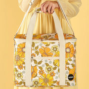 Photographed in front of a yellow background is a picnic bag with cream straps and 70's style yellow and orange floral print.