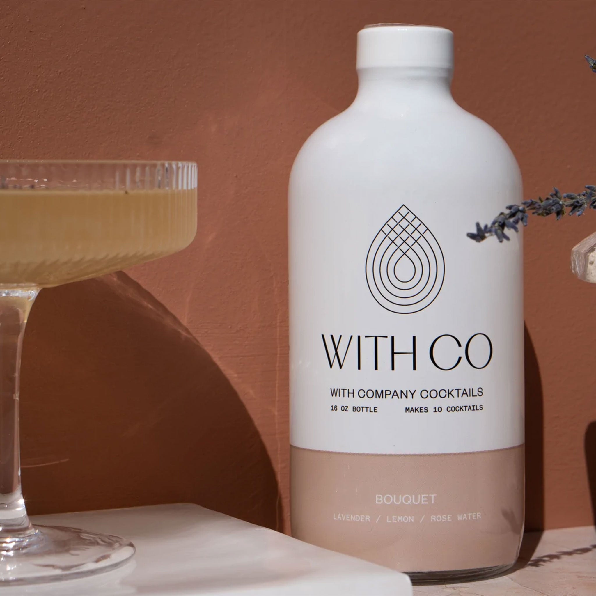 A white bottle of cocktail mix with a neutral blush bottom half and writing in the center of the bottle that says, &quot;With Co Cocktails&quot;.