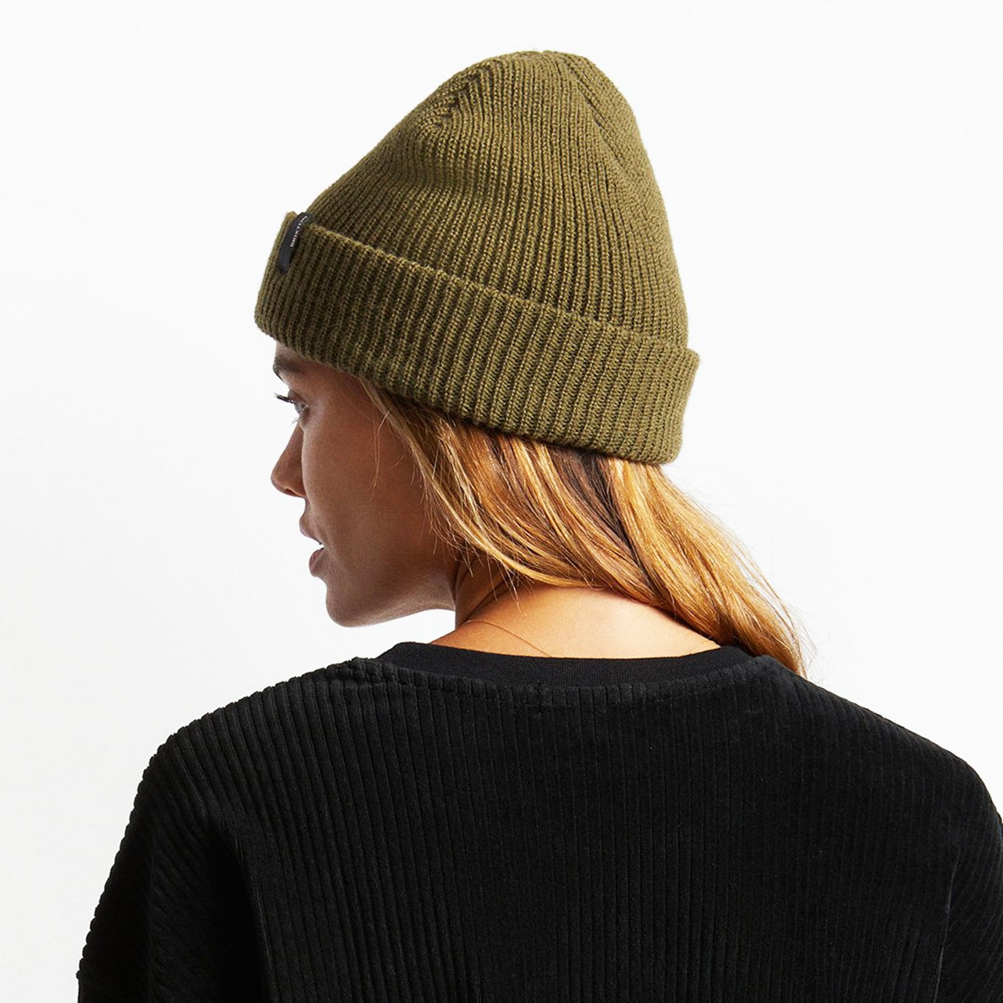 An olive green knit beanie with plush acrylic and has a folding cuff detailed with a woven label. 