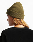 An olive green knit beanie with plush acrylic and has a folding cuff detailed with a woven label.