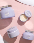 Four different sized and shaped glass candle jars in a lavender purple color. Each has a circular label that reads, "Volcano".