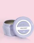 A small lavender tin candle with white wax and a white diamond repeating pattern on the outside of the tin. Comes with a matching purple lid that reads, "Capri Blue Volcano".