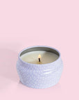 A small lavender tin candle with white wax and a white diamond repeating pattern on the outside of the tin. Comes with a matching purple lid that reads, "Capri Blue Volcano".