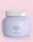 The larger of the two glass candle jars in a lavender purple shade along with a silver lid and a circle label in the center that reads, "Capri Blue, Volcano 06".