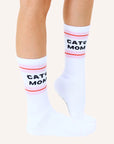 White crew socks with a pink and red striped design at the top along with black text that reads, "Cat Mom" as well as a small black paw print next to the word "cat".