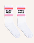 White crew socks with a pink and red striped design at the top along with black text that reads, "Cat Mom" as well as a small black paw print next to the word "cat".