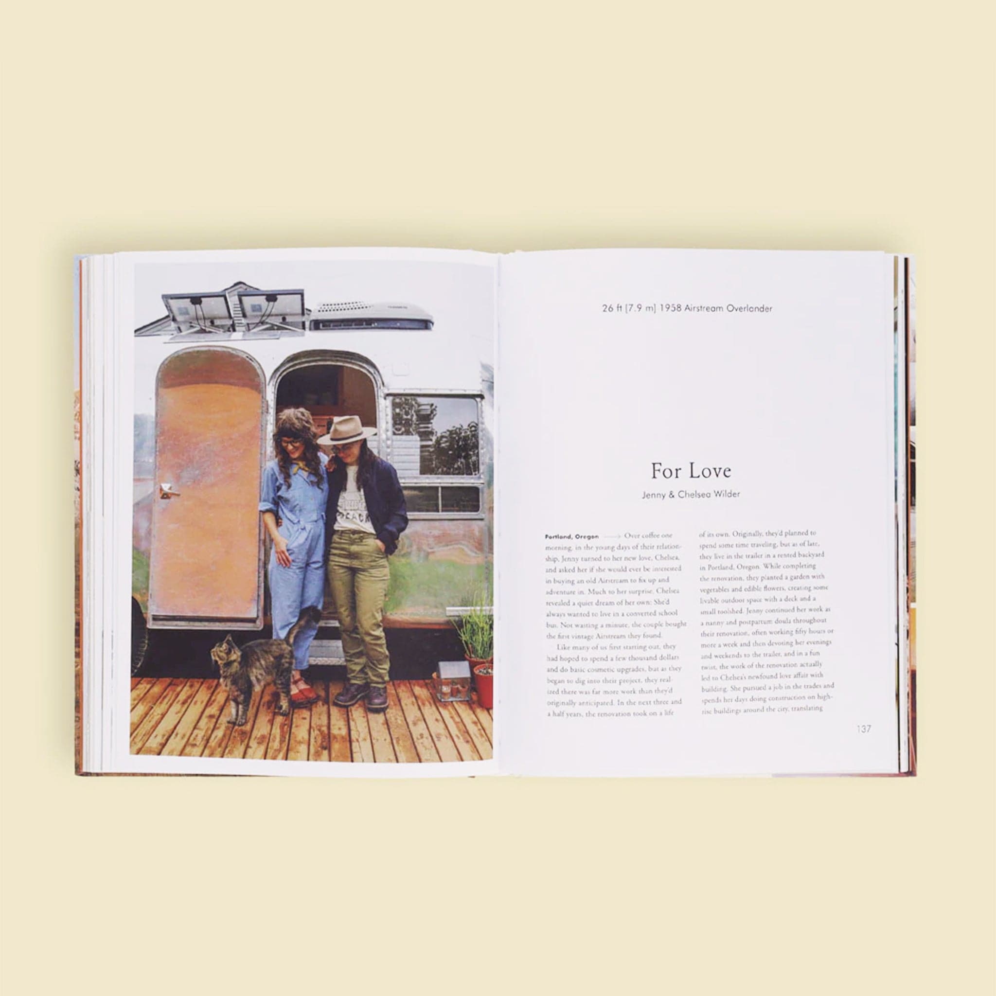 Two open pages of the book. The left page is filled with a sweet couple looking down at their long haired cat, posed in front of their silver airstream trailer. The right page is titles &#39;For Love&#39; and dives into the story of Jenny and Chelsea Wilder against a solid white page. 