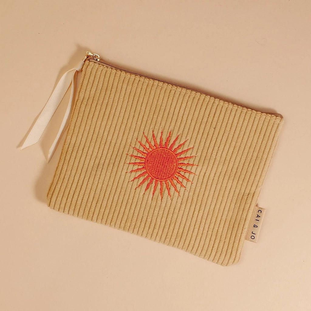 A pastel green corduroy pouch with an orange sun design in the center along with a single zipper going across the top that is detailed with a white ribbon.