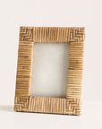 In front of a white background is a rattan picture frame. The corners of the picture frame are a chevron design and the sides are stripes.