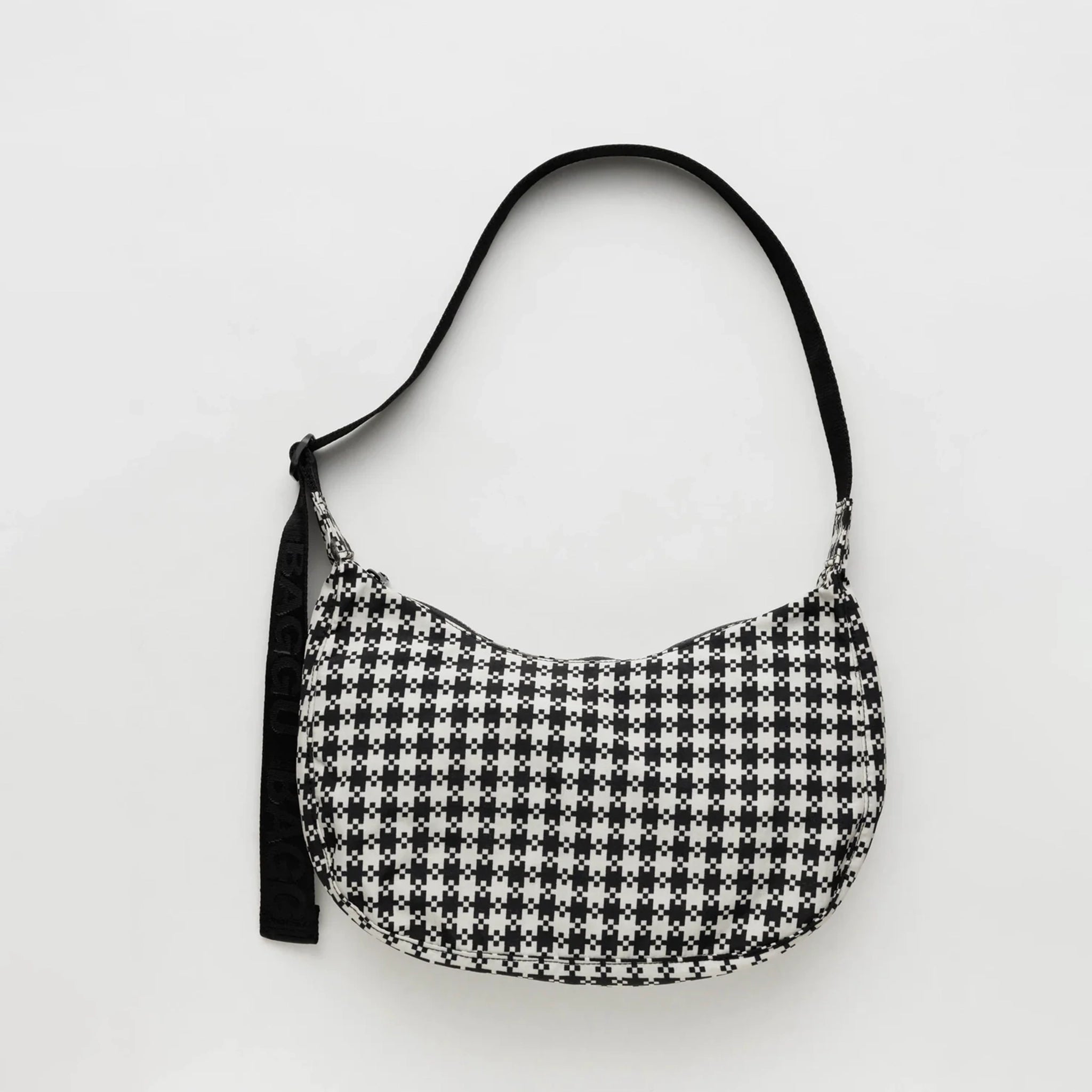 A black and white gingham nylon crescent shaped bag with an adjustable black strap that reads, "BAGGU" in black and a single zipper.