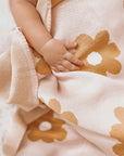 A light blush cotton blanket with a repeating mustard yellow daisy print.