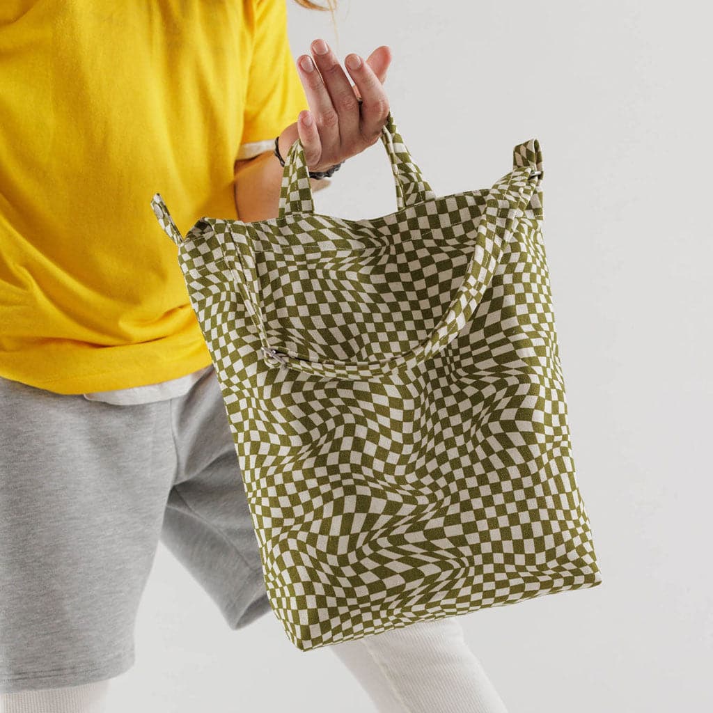 Woman holding the moss checkered tote in her hand. The woman is wearing a bright yellow shirt and grey sweat shorts. 