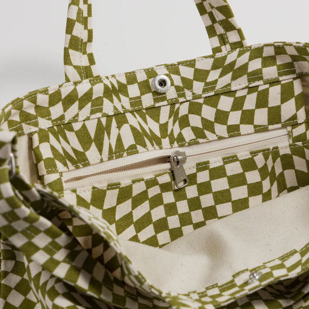 Close up of the interior of the tote. A side zipper is shown unzipped slightly. A metal clasp is position below the small handles, stitched at the top of the bag. 