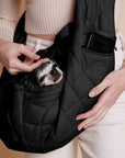 A black quilted puffer material crossbody pet carrier bag photographed with a small black and white dog in it and a zipper that fits an iPhone.