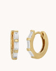Gold huggie hoop earrings featuring baguette style cubic zirconias along the gold huggie earring.