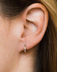 A small huggie hoop earring worn on a model's ear and features baguette style cubic zirconias along the gold huggie earring.