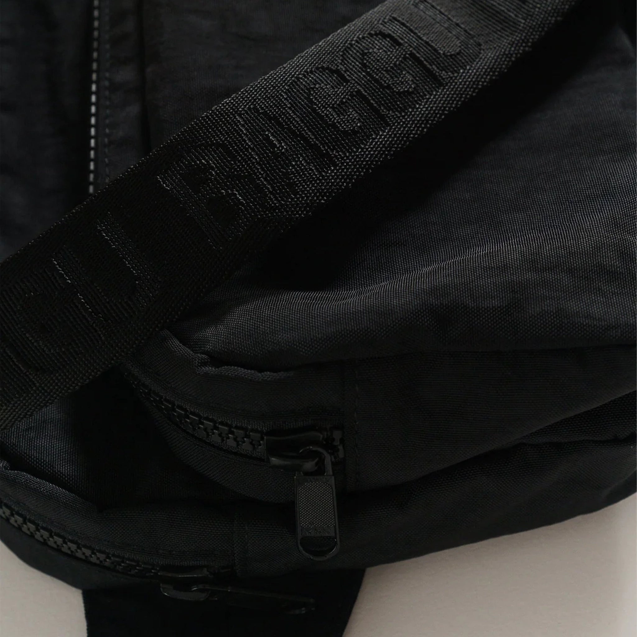 A black nylon fanny pack with two zipper pockets and a black adjustable strap.
