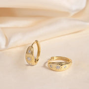 Gold huggie hoop earrings with edged starbursts with three CZ stones along the front.