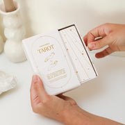 A cream box of 78 Tarot cards with an illustration of two hands and a star in between. All cards are beautifully illustrated with descriptions underneath and detailed with gold foiling.