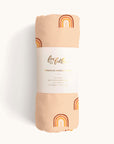Peach swaddle covered in a warm toned rainbow pattern wrapped in white packaging that reads 'fox and follow, premium muslim wrap' in gold foil text.