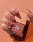 A rosie nail polish with a satin finish in a glass bottle with a peachy square lid.