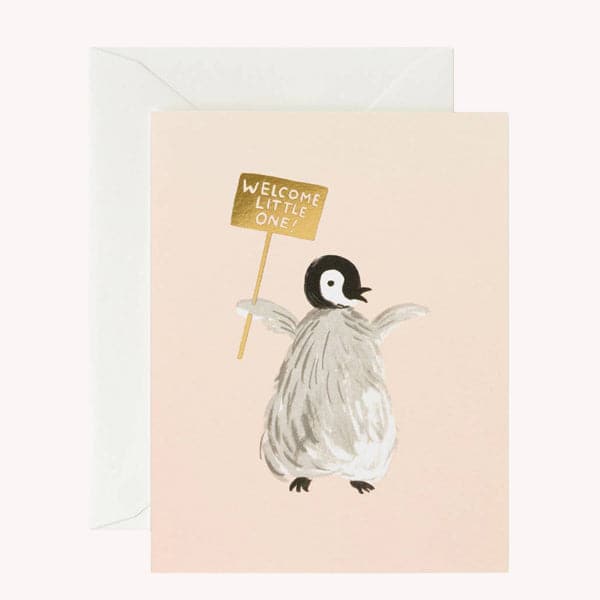 This adorable card is the color of a peach cloud. In the center is a grey feathery penguin chick holding a reflective gold sign labeled &#39;Welcome Little One&#39;. The card is accompanied by a solid white envelope.