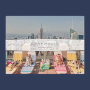 A puzzle in a box with a photograph of New York City with different breeds of dogs wearing sunglasses and sitting on a rooftop on sun chairs.