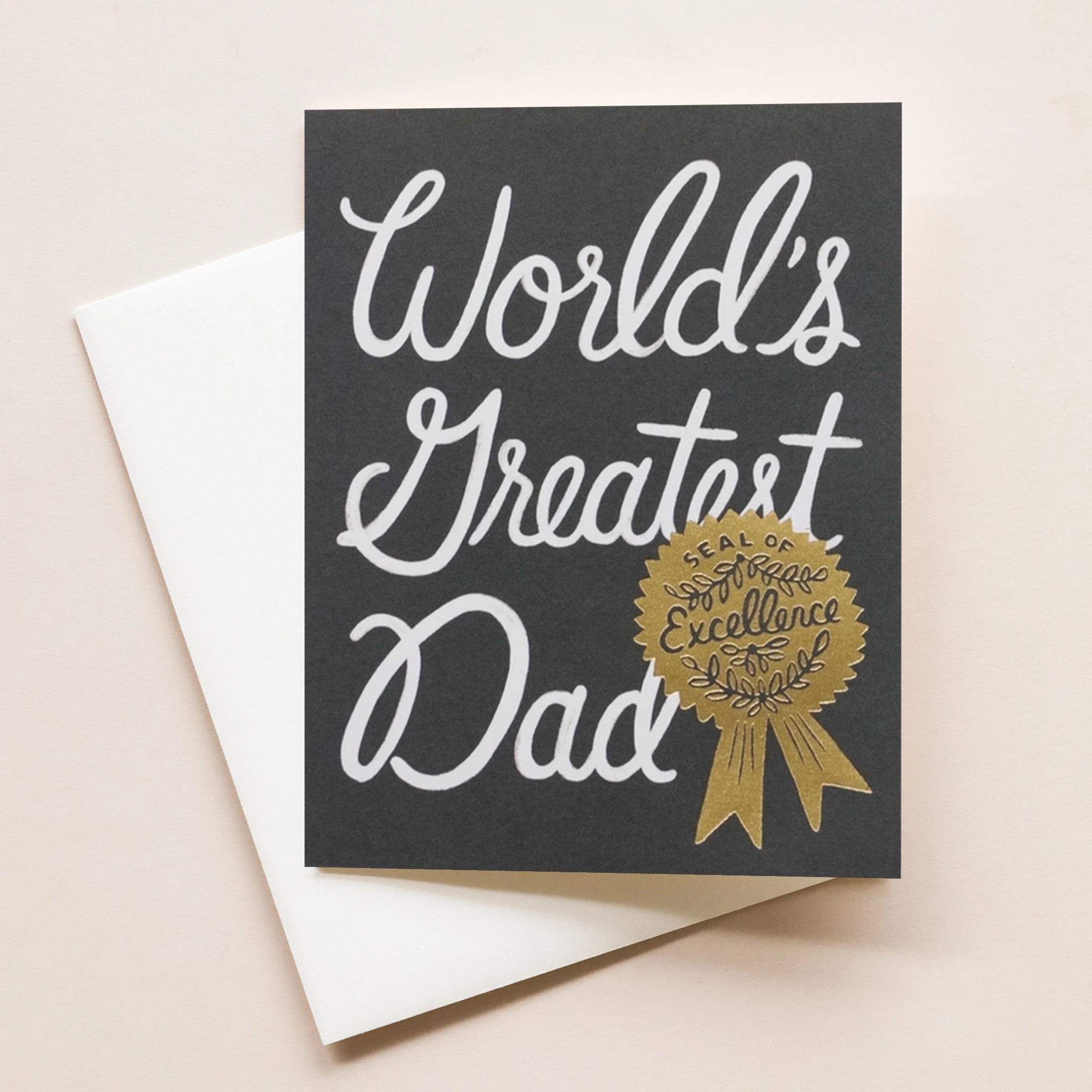 This card reads 'World's Greatest Dad' in white cursive over a black background. Along side the text is a metallic gold award-shaped 'Seal of Excellence'. The text is accompanied by a white envelope.
