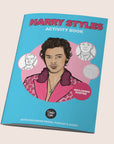 A blue coloring book with a graphic of Harry Styles in a pink polka dot suit along with pink text on the top that reads, "Harry Styles Activity Book".