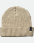 A knit ribbed beanie in a beige color with a folded brim and a black label on the front right left corner.