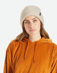A knit ribbed beanie in a beige color with a folded brim and a black label on the front right left corner.