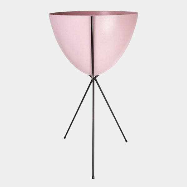In front of a white background is a pink colored bullet planter. The planter has a wide top and narrows at the bottom. The planter is held up by a black metal stand. The stand has three black metal legs.