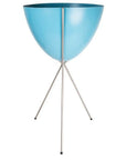 In front of a white background is a bright blue colored bullet planter. The planter has a wide top and narrows at the bottom. The planter is held up by a silver metal stand. The stand has three silver metal legs.