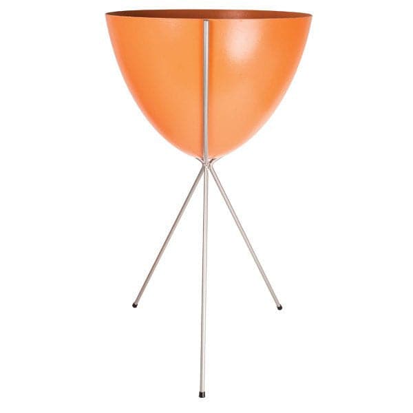 In front of a white background is an orange colored bullet planter. The planter has a wide top and narrows at the bottom. The planter is held up by a silver metal stand. The stand has three silver metal legs.
