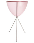 In front of a white background is a pink colored bullet planter. The planter has a wide top and narrows at the bottom. The planter is held up by a silver metal stand. The stand has three silver metal legs.