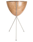 In front of a white background is a wood colored bullet planter. The planter has a wide top and narrows at the bottom. The planter is held up by a silver metal stand. The stand has three silver metal legs.