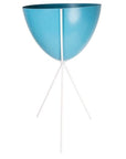 In front of a white background is a blue colored bullet planter. The planter has a wide top and narrows at the bottom. The planter is held up by a white metal stand. The stand has three white metal legs.