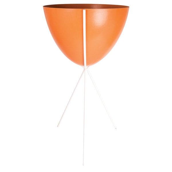 In front of a white background is an orange colored bullet planter. The planter has a wide top and narrows at the bottom. The planter is held up by a white metal stand. The stand has three white metal legs.